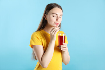 Woman drinking juice through straw on light blue background