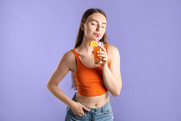 Woman drinking juice through straw on violet background