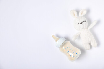 Feeding bottle with formula and toy rabbit on light background, flat lay. Space for text