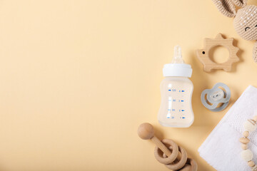 Bottle with milk and baby accessories on beige background, flat lay. Space for text