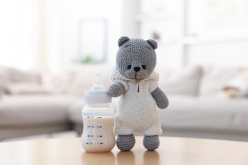 Baby bottle with milk and toy bear on table indoors