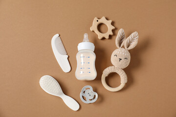 Bottle with milk and baby accessories on brown background, flat lay