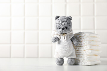 Baby diapers and toy bear on white table near tiled wall. Space for text