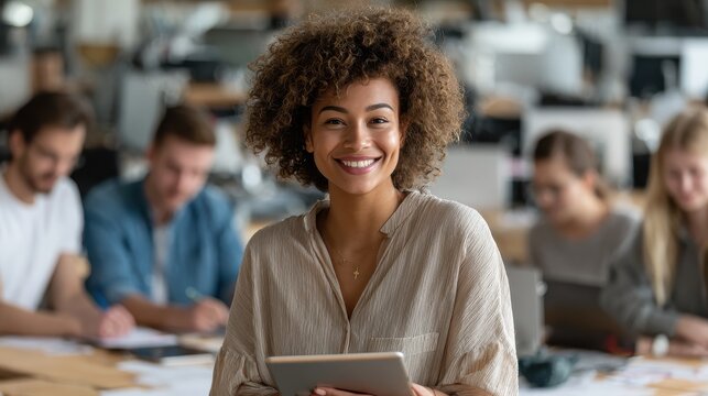 young happy african american woman team leader sitting on desk holding tablet and international business startup students working studying at desk on project in contemporary classroom office portrait
