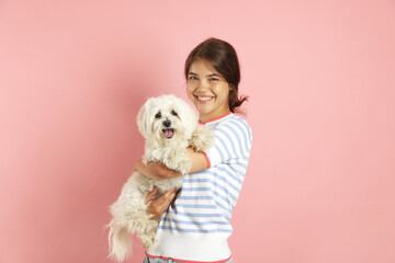 Happy teenage girl with Maltese dog on pink background