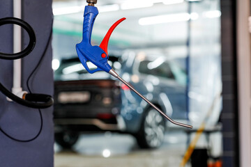 A blue and red air blow gun hangs in a service garage. In the background, vehicles are getting...