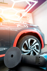 A detailer readies a polishing tool in a garage setting. A black car with orange accents awaits...