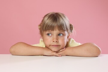 Curious little girl peeking over table against pink background