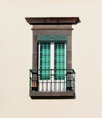 Obraz premium Classic window with green shutters and small balcony on a beige wall. Mediterranean architectural detail with iron railing and stone frame.