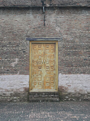 A wooden door with intricate square patterns set in an old, textured brick wall.