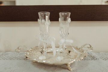 Set on a beautifully adorned table, two delicate champagne flutes stand ready for a toast, embellished with floral designs and accompanied by a silver tray.