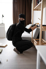 Burglar, robber or thief breaks home. Woman wearing black balaclava stealing things searching money...