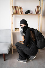 Female Burglar or thief in black balaclava stealing money from apartment showing shh silence...