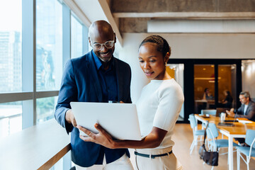 Two colleagues discussing a project and viewing a laptop in an office setting