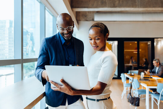 Two colleagues discussing a project and viewing a laptop in an office setting - Powered by Adobe