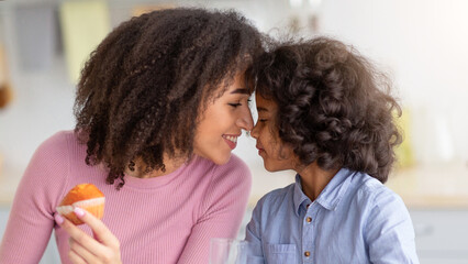 Love And Tenderness. Portrait Of Cute Little Black Girl Having Breakfast Together With Smiling Woman, Relatives Touching Foreheads, Sitting At Dinner Table In Kitchen, Eating Cookies Drinking Milk