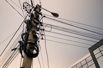 Utility pole with tangled overhead cables and streetlight against modern glass building background