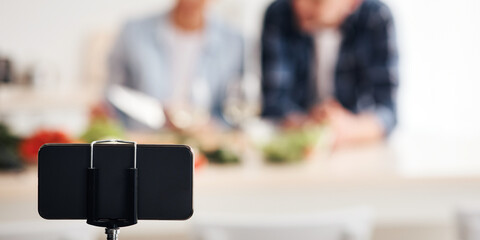 Blogger job and shoot video on webcam. Couple cook, recording live video for vlog and social media with mobile phone on tripod. Happy adult wife and husband prepare food in kitchen interior, blurred