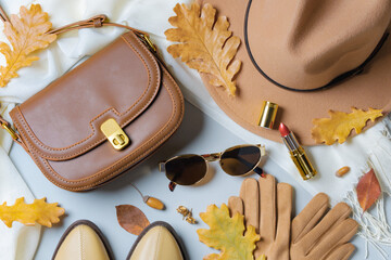 Autumn accessories flat lay. Brown hat, leather bag, gloves, shoes with pumpkins and colorful...