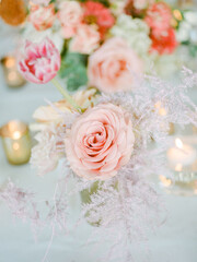 Elegant floral arrangement featuring roses and tulips in soft hues with candles illuminating the setting