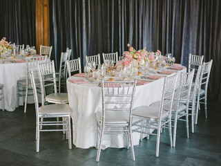 Elegant round tables set for a wedding reception with floral centerpieces and silver chairs at a beautifully decorated venue