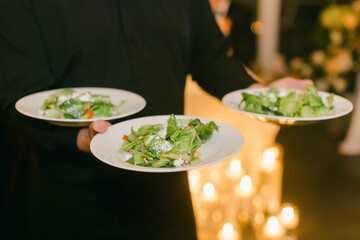 Waitstaff serving three fresh salads at an upscale event during an evening gathering with elegant...