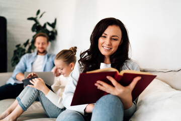 Father types on laptop while daughter shows tablet to mother, creating tech-assisted learning triangle and showcasing intergenerational digital engagement.