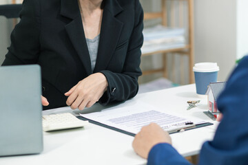 car dealership is talking with customer in their office to offer promotions and deals as they sign sales contract. contract document is laid out on table in dealership office ready for customer sign.
