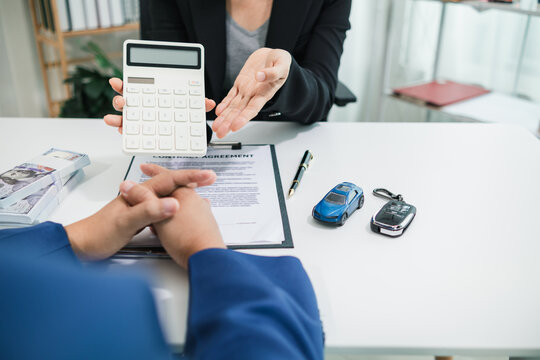 car dealership is talking with customer in their office to offer promotions and deals as they sign sales contract. contract document is laid out on table in dealership office ready for customer sign.