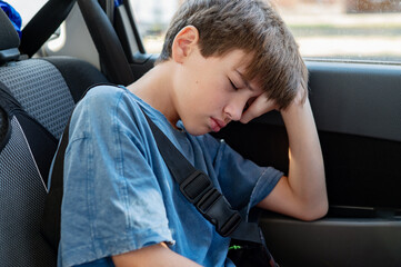 A disgruntled, half-asleep teenager leans against the window in the back seat of a car