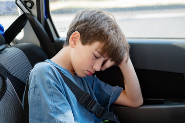 A disgruntled, half-asleep teenager leans against the window in the back seat of a car