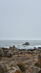 Fog covers the rocky Atlantic coast in Leça da Palmeira, Matosinhos, Portugal, as waves crash against rugged stones on a rough sea day. The dramatic seascape evokes nature’s power and coastal solitude