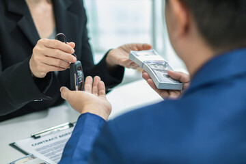 buyer is receiving the car keys from the car dealer after completing the sales contract and paying the dealer. dealer hands the car keys to the customer in the office after completing sales contract.