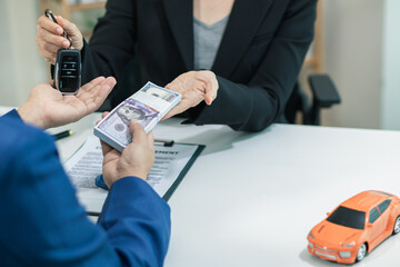 buyer is receiving the car keys from the car dealer after completing the sales contract and paying...