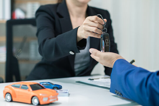 buyer is receiving the car keys from the car dealer after completing the sales contract and paying the dealer. dealer hands the car keys to the customer in the office after completing sales contract.