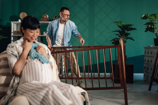 Father bringing baby crib to pregnant wife in nursery