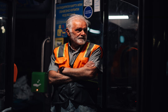 Senior bus driver wearing safety vest waiting at night inside public transportation vehicle