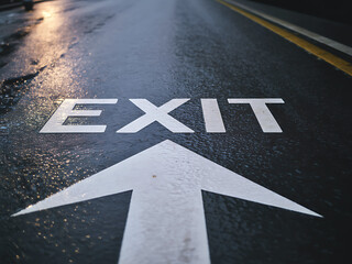 Wet asphalt road with white exit sign and arrow pointing forward