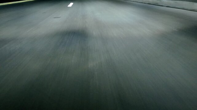 Low angle POV asphalt road with lane markings. Night
