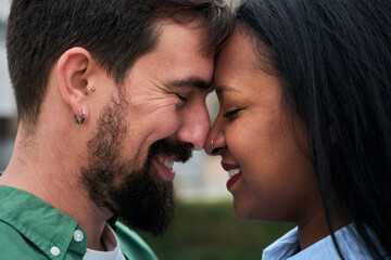 A close-up of an interracial couple sharing an intimate moment with foreheads touching, eyes closed and smiling, expressing tenderness, trust and deep connection.