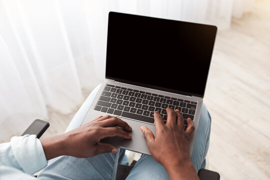 Covid-19 quarantine and modern work at home, education and blog. Mature african american man disabled in wheelchair typing on laptop with empty screen in living room interior, pov, cropped, copy space