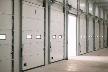 Interior view of a modern warehouse loading bay with multiple numbered sectional overhead doors. The facility is designed for logistics, freight handling, cold storage operations, and efficient supply