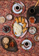 Coffee table setting with white cups, red and gold bordered plates on oriental patterned tablecloth.