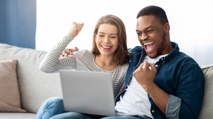 Happy Excited Interracial Couple Celebrating Success With Laptop At Home, Lucky Multicultural Spouses Looking At Computer Screen, Shaking Clenched Fists And Exclaiming With Excitement, Closeup