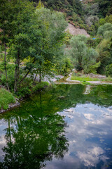 Serene pond reflecting trees and sky, surrounded by lush greenery and hills in Başiskele, Kocaeli, Türkiye, creating a peaceful natural scene.