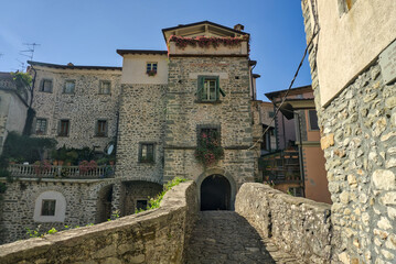 A view of a narrow, historic street in a stone village, with an arched walkway connecting the...