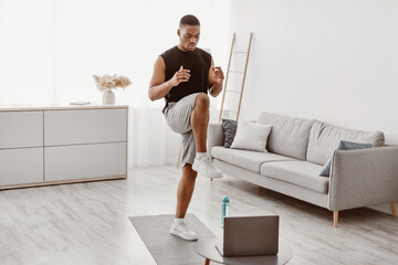 Online Fitness. Sporty Black Man Doing Standing Knee Raise Exercise At Laptop Training During...