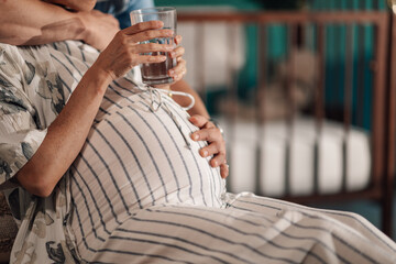 Pregnant woman holding glass of water near baby crib