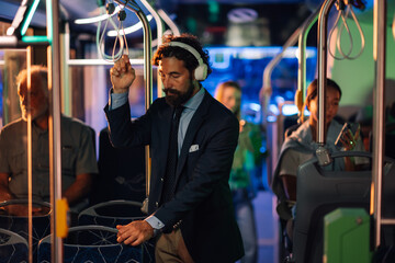 Businessman listening music with headphones on bus at night