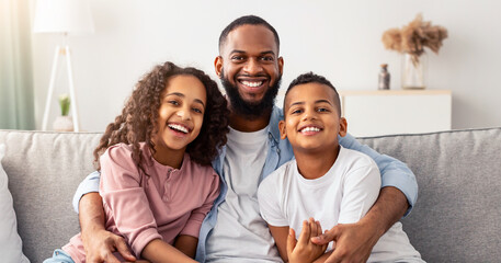 Happy Loving Family. Portrait of cheerful smiling African American dad embracing his little children, sitting on couch, looking at camera. Girl, boy and man hugging, enjoying time together